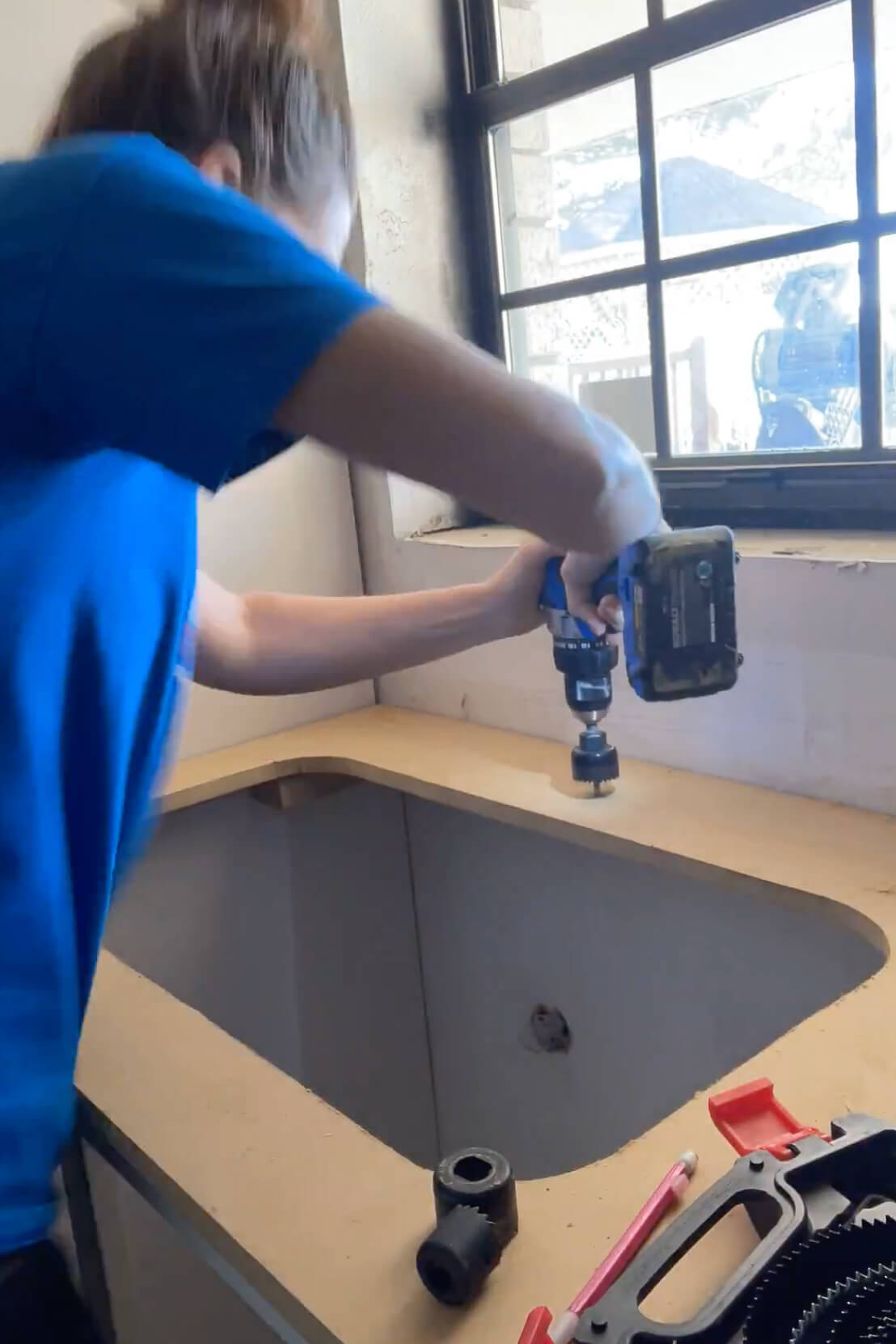 Using a hole saw to cut holes in a kitchen counter for a kitchen faucet.